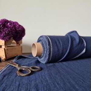 May include: A roll of dark blue fabric sits next to a pair of vintage scissors. A wooden crate holds a cluster of purple flowers. Two spools of thread, one pink and one blue, are also visible.