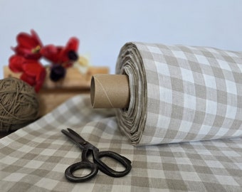 May include: A roll of beige and white gingham fabric with a cardboard core. The fabric is lying on a table with a pair of scissors and a ball of twine.