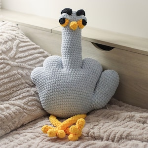 Peut inclure: Un jouet en peluche crocheté en forme de majeur avec une tête d'oiseau et des pattes jaunes. Le jouet est bleu clair avec des yeux noirs et un bec jaune.