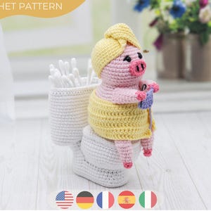 May include: A crocheted pig ornament, seated on a toilet, wearing a yellow towel and head wrap. The pig is holding knitting needles and yarn. A white crochet container holds cotton buds. The text "CROCHET PATTERN" is at the top.