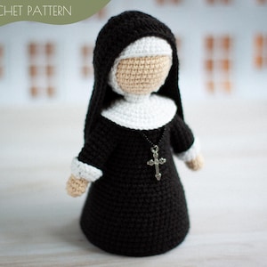 以下が含まれることがあります： 黒い習慣、白いベール、銀の十字架のネックレスをつけた、かぎ針編みの修道女の人形。人形は、中立的な表情のかぎ針編みの顔をしています。
