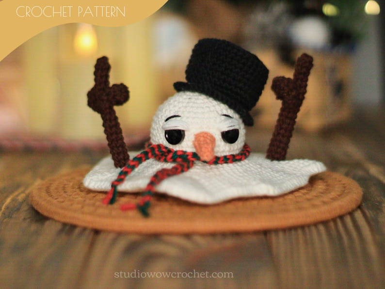 May include: A crocheted snowman with a black top hat and red and green scarf, melting on a brown crocheted coaster. The snowman has black eyes and a small orange nose.