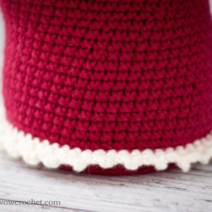 May include: A close-up of a red crocheted hat with a white crocheted trim around the bottom edge.