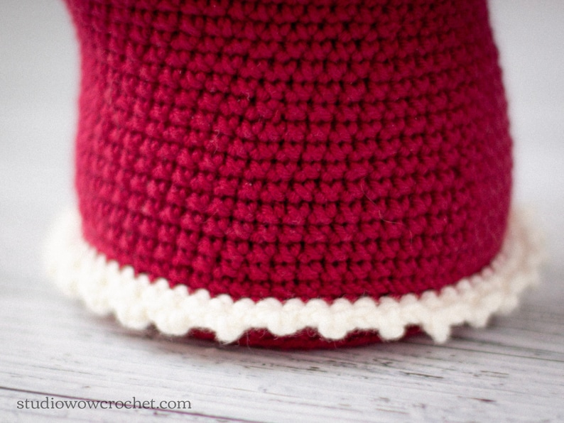 May include: A close-up of a red crocheted hat with a white crocheted trim around the bottom edge.