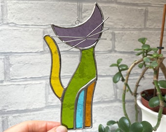 May include: A stained glass cat suncatcher with a purple head, green body, yellow tail, and blue and orange accents.