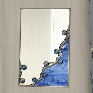 May include: A rectangular mirror with a blue and silver design. The mirror has a wavy edge with blue glass and silver metal accents. The design features small blue glass spheres.