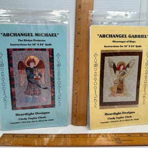 May include: Two Heartlight Designs quilt pattern packets, Archangel Michael and Archangel Gabriel, each for a 16 inch by 24 inch quilt. The packets are in clear plastic sleeves next to wooden rulers showing measurements in inches.