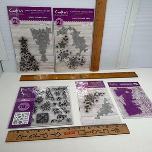 May include: A collection of Crafter's Companion clear stamp and metal die sets, including Holly Flower Tree, Holly Flower Arch, and Season's Greetings. The items are displayed with wooden rulers showing measurements in inches.