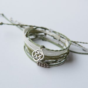May include: A stack of green and white braided bracelets with a silver charm in the shape of a Celtic knot.