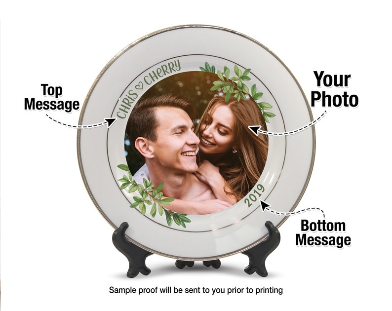 May include: A white ceramic plate with a gold rim, displaying a couple's photo surrounded by green foliage. The plate has the text "CHRIS & CHERRY" and "2019". It is displayed on a black stand.