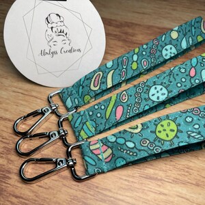 May include: Three teal blue keychains with a colourful pattern of bacteria and other microorganisms. Each keychain has a silver metal lobster clasp.