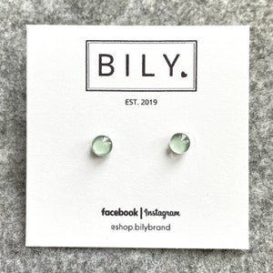 May include: A pair of light green stud earrings on a white card. The card has the brand name "BILY." in a black box, with "EST. 2019" below. Social media handles are listed at the bottom: facebook | Instagram @shop.bilybrand.