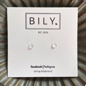 May include: A white card with the text "BILY." and "EST. 2019" printed on it. Two small, clear, round stud earrings are displayed on the card. The text "facebook | instagram @shop.bilybrand" is printed at the bottom of the card.