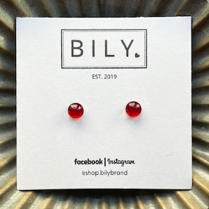 May include: A pair of small, round, red stud earrings on a white card. The card has the brand name "BILY." in a black box, with "EST. 2019" below. Social media handles are listed at the bottom.