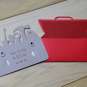 May include: A gray card shaped like a toolbox with cut-out tool silhouettes and the text "thanks for being the BEST dad we love you." A red toolbox-shaped card is open next to it.