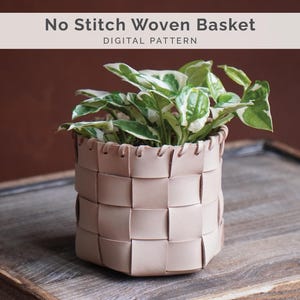Puede incluir: Una cesta tejida de cuero de color beige claro, que contiene una planta verde y blanca. La cesta tiene un patrón de tejido cuadrado y es cilíndrica. El texto "No Stitch Woven Basket" y "Digital Pattern" está en la parte superior.