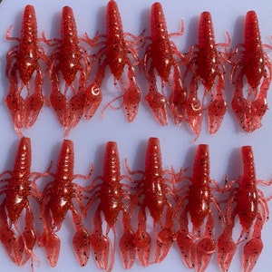 May include: Ten red crawfish-shaped fishing lures with black speckles. The lures have segmented bodies and articulated claws.