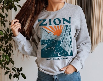 May include: A gray sweatshirt with a graphic print of a mountain landscape and the text "Zion National Park".