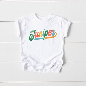 May include: White t-shirt with the word "Juniper" written in a colorful retro font.