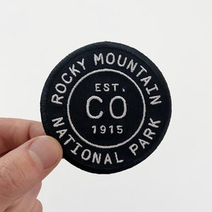 May include: Black and white embroidered patch with the text "Rocky Mountain National Park Est. 1915 CO" in a circle.