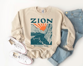 May include: A beige sweatshirt with a graphic print of a mountain landscape and the text "Zion National Park".