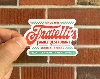 May include: A red and green sticker with the text "Fratelli's Family Restaurant" and the tagline "Astoria - Oregon" with the words "Pizza - Ice Cream - Water - Tongue" below.