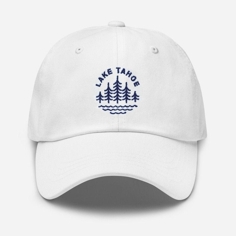 May include: White baseball cap with a navy blue embroidered logo that says "LAKE TAHOE" with a circle of pine trees and a wavy line representing water.