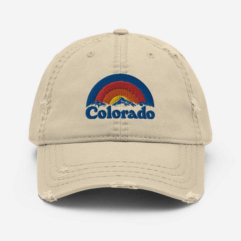 May include: A beige distressed baseball cap with a vintage-style embroidered design featuring a rainbow arch over mountains and the word "Colorado" in blue.
