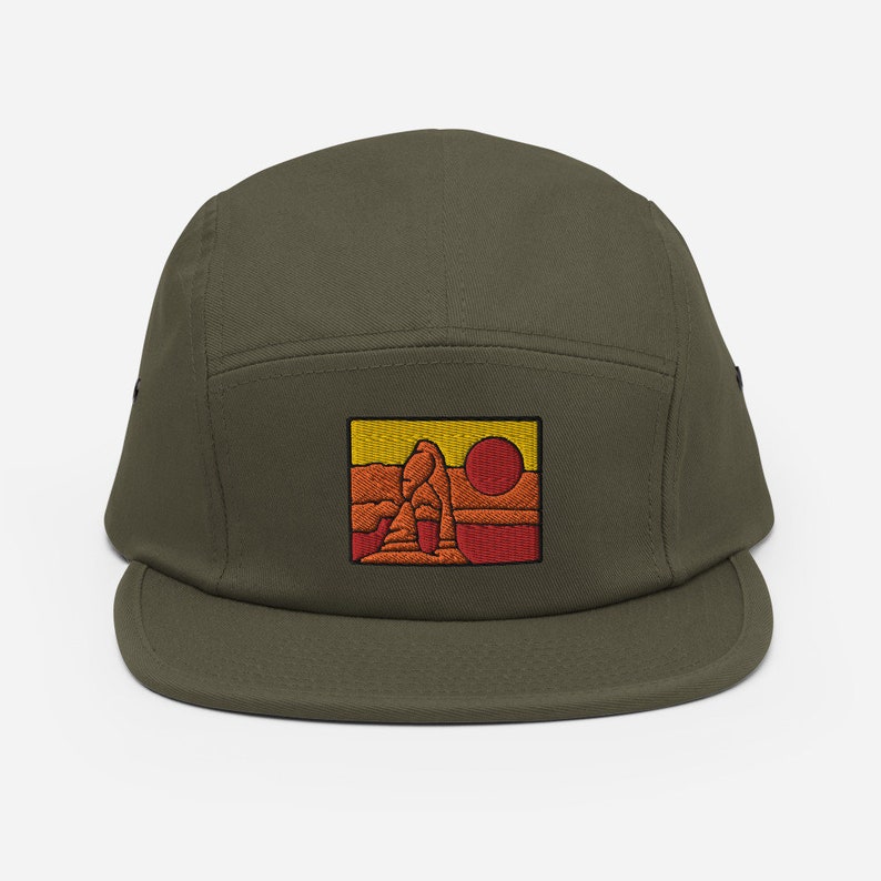 Puede incluir: Una gorra verde de 5 paneles con un parche bordado de un paisaje des&eacute;rtico con un sol rojo y una formaci&oacute;n rocosa amarilla.