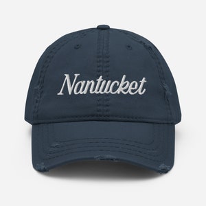 Può includere: Cappellino da baseball blu navy con la scritta "Nantucket" ricamata in bianco. Il cappellino ha un aspetto invecchiato con bordi sfilacciati, che suggerisce uno stile vintage o casual.
