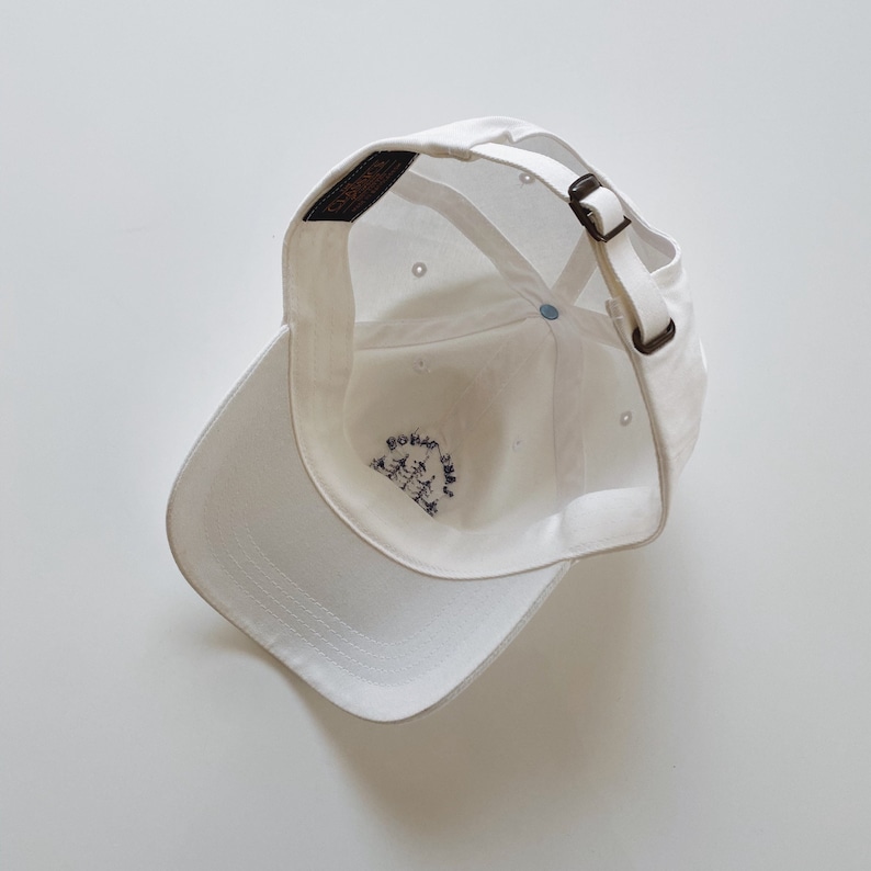 May include: White baseball cap with an adjustable strap and a small embroidered logo on the inside.