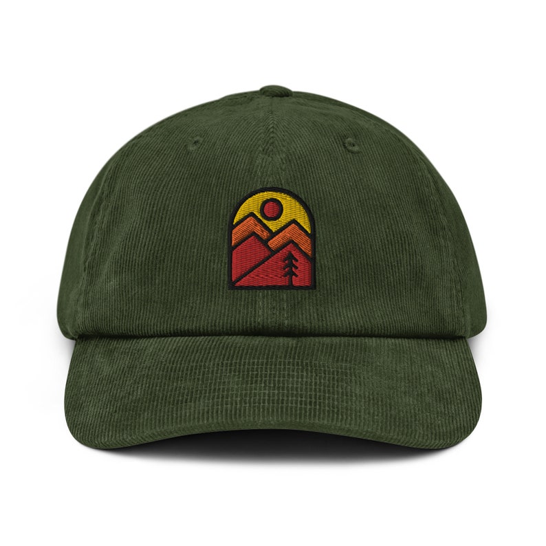 May include: A green corduroy baseball cap with an embroidered patch of a mountain range with a sun and a tree. The patch is in shades of red, orange, and yellow.