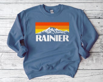 May include: A blue sweatshirt with a retro-style graphic of Mount Rainier and the text "RAINIER" in white.