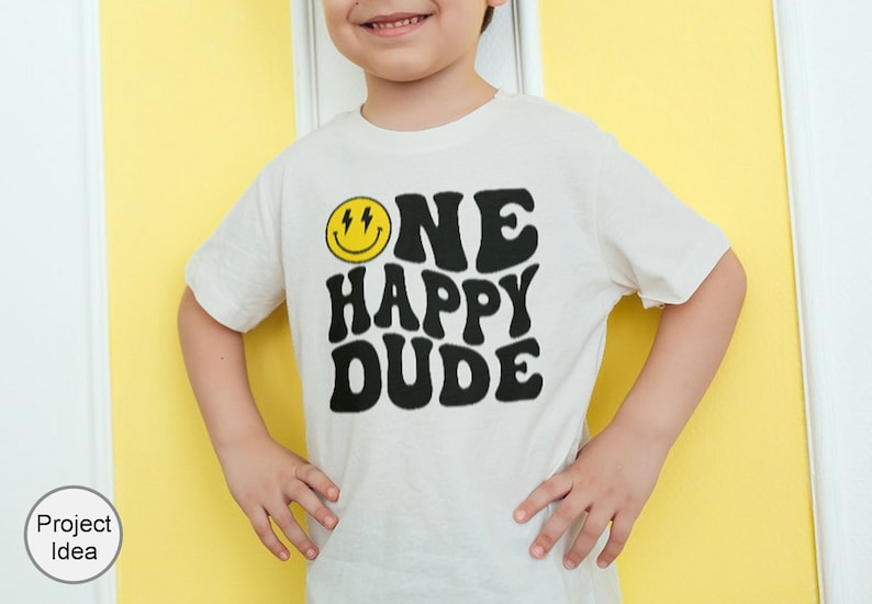 Pu&ograve; includere: Una maglietta bianca con una grafica nera che dice "ONE HAPPY DUDE" in un font retr&ograve;. Un viso sorridente giallo con fulmini &egrave; sopra il testo.