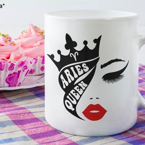K&ouml;nnte beinhalten: Wei&szlig;e Keramiktasse mit einer schwarz-wei&szlig;en Grafik eines Frauenkopfes mit einer Krone und dem Text "Aries Queen".