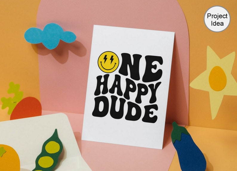 Pu&ograve; includere: Un biglietto bianco con testo nero che recita "ONE HAPPY DUDE" in un font retr&ograve;. Sopra il testo c'&egrave; un'emoticon gialla con fulmini per gli occhi.