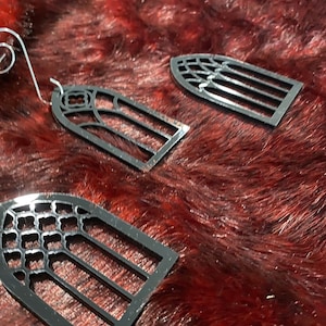 May include: Three black metal ornaments shaped like arched windows with different patterns. The ornaments are on a red fuzzy surface.