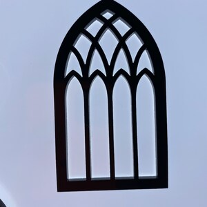 May include: Black wooden cutout of a gothic arch window with three panes. The window has a decorative design with multiple points.