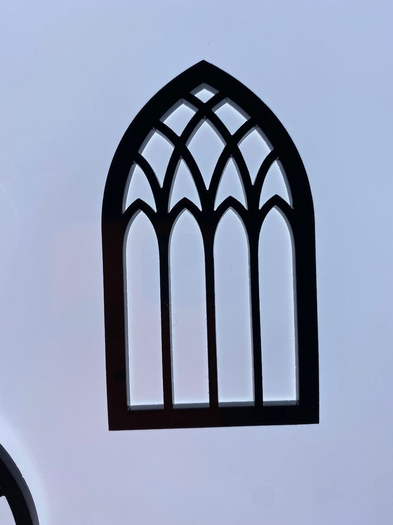 May include: Black wooden cutout of a gothic arch window with three panes. The window has a decorative design with multiple points.