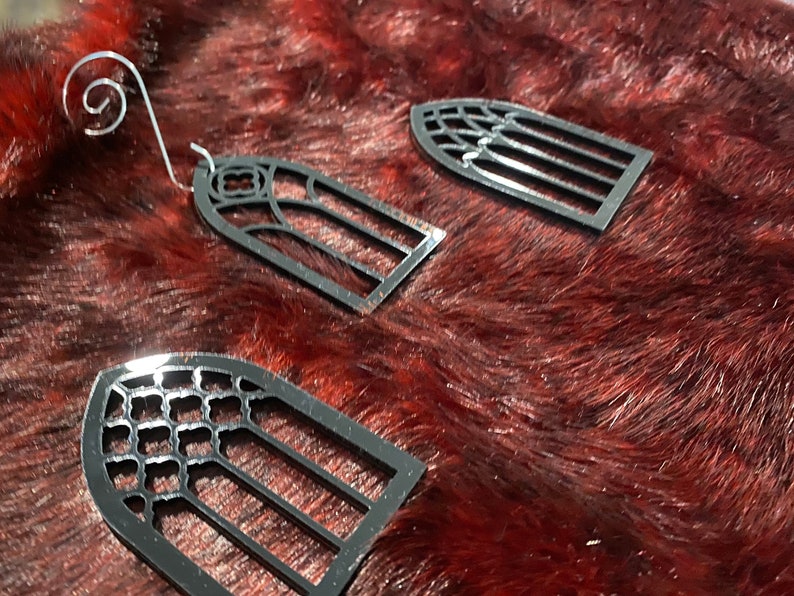 May include: Three black metal ornaments shaped like arched windows with different patterns. The ornaments are on a red fuzzy surface.