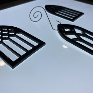 May include: Two black metal window ornaments with a decorative design. The ornaments are shaped like arched windows with a grid pattern.