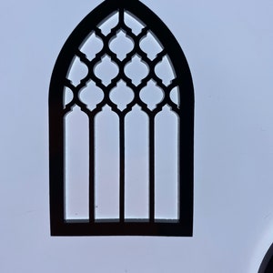May include: Black wooden cutout of an arched window with a geometric lattice design. The window has four vertical panes and a pointed arch.