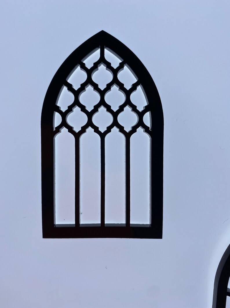 May include: Black wooden cutout of an arched window with a geometric lattice design. The window has four vertical panes and a pointed arch.