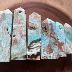 May include: Six blue and brown banded crystal points, also known as Celestite, arranged in a row on a wooden surface.