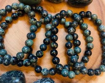 May include: Three green and black gemstone bracelets with matching tumbled stones. The bracelets are made of round beads and the stones have a marbled pattern.