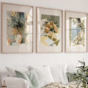 May include: Three framed watercolor prints depicting botanical and coastal scenes. The prints feature a vase with a plant, lemons on a table, and a coastal view through a window. The frames are light-colored wood, and the overall aesthetic is bright and airy.