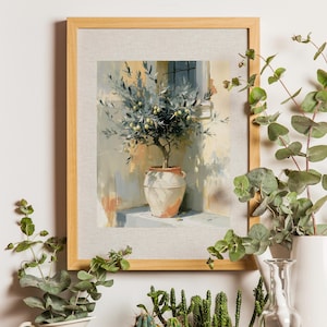 May include: A framed art print depicts an olive tree in a terracotta pot. The painting has a light color palette with a beige frame. The artwork is surrounded by greenery, including eucalyptus and cacti, creating a natural, decorative display.