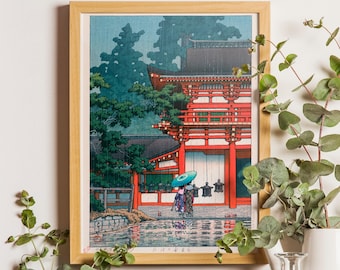 May include: A framed woodblock print depicting a vibrant red temple structure amidst dark green trees during a rainstorm. A figure holding a bright blue umbrella stands near the temple entrance, with reflections visible in the water below.