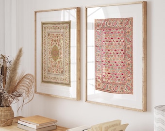 May include: Two framed rectangular wall art pieces. One features a beige and green floral pattern, the other a pink and red floral design. Both are framed in light wood and hang on a white wall. The art pieces are above a wooden table with books and decorative items.