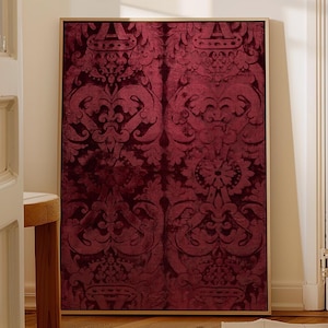 May include: A framed burgundy wall art piece with a gold frame. The artwork features a repeating pattern of ornate floral and scroll designs. The color palette is a deep burgundy with darker accents, creating a rich, textured appearance.
